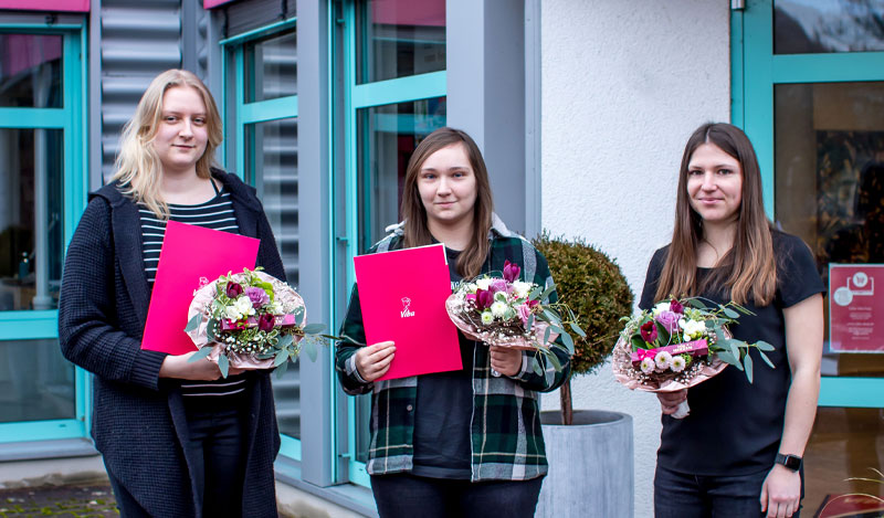 Drei Absolventinnen bei Übergabe der Blumensträuße