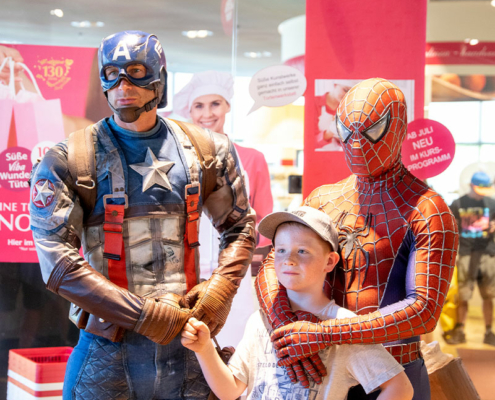 Captain America und Spider-Man posieren mit einem Jungen vor dem Shop der Nougat-Welt