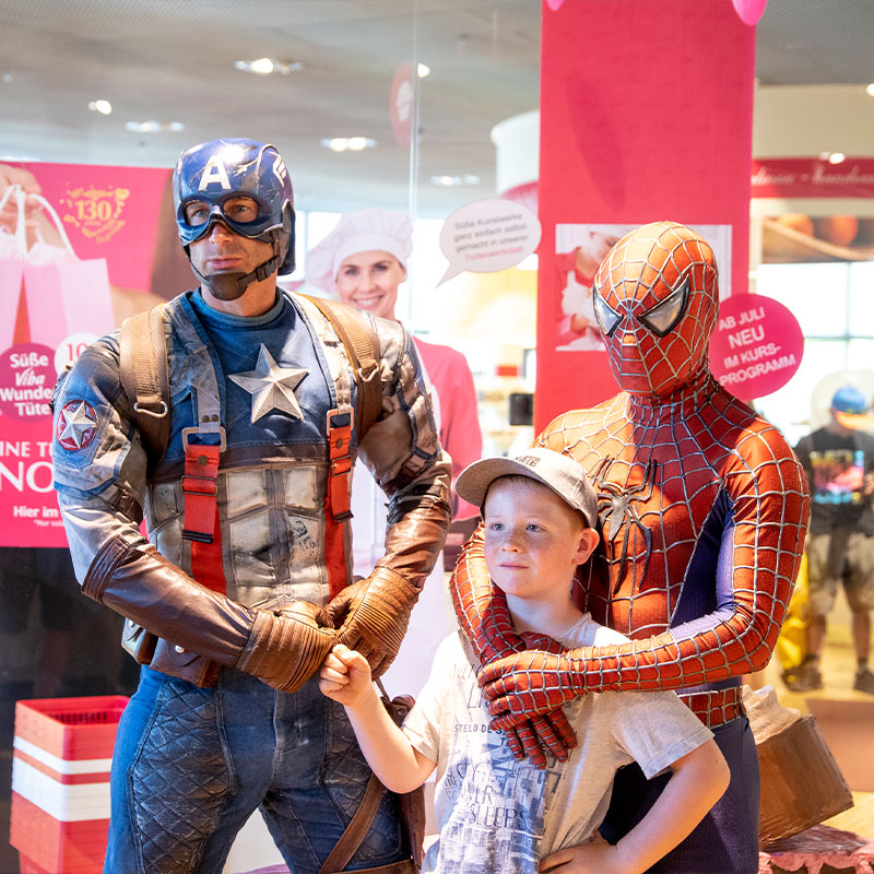 Captain America und Spider-Man posieren mit einem Jungen vor dem Shop der Nougat-Welt